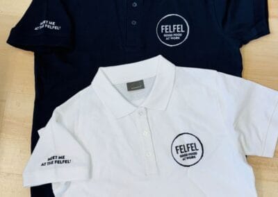 Zwei Poloshirts, eins in Schwarz und eins in Weiß, mit dem "FELFEL" Logo. Perfekt für Arbeit und Freizeit mit stilvollem Design.