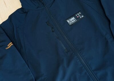 Marineblaue Jacke mit Reißverschluss auf hellem Holzboden. Stickerei auf den Ärmeln verleiht einen coolen und sportlichen Look. Perfekt für den Alltag!